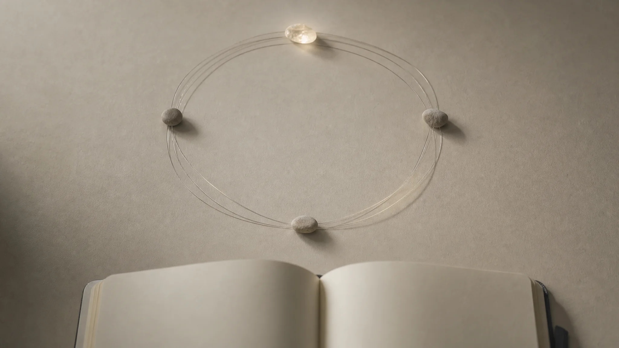 A faint circular thread loop connects small stones above an open notebook, evoking a repeating pattern traced across time.
